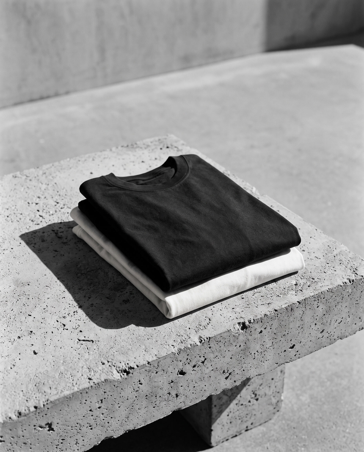 Folded black and off-white heavyweight tees on concrete